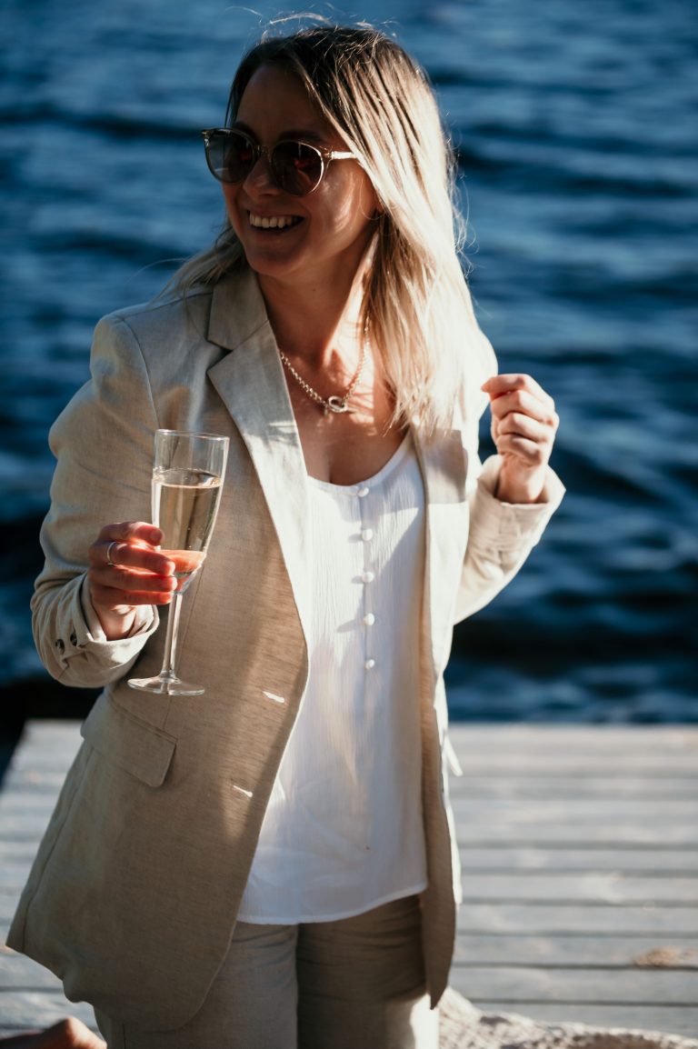 Influencer Theodora Larsson på en brygga vid vatten med champagneglas i handen.